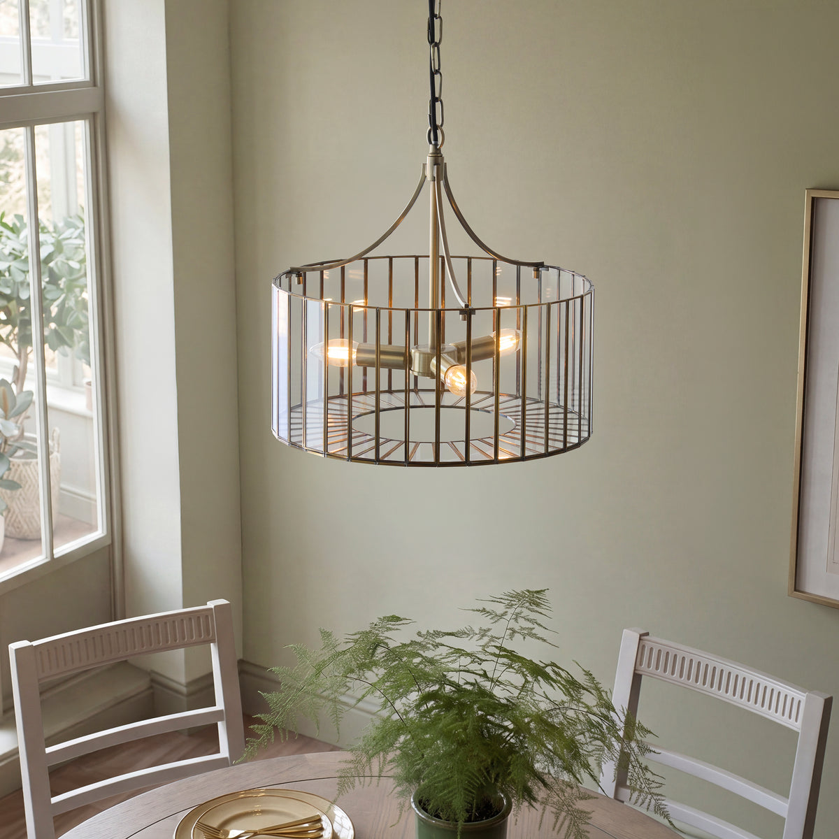 Lit Antalya brass cage pendant over a dining table set with plates in a soft green interior