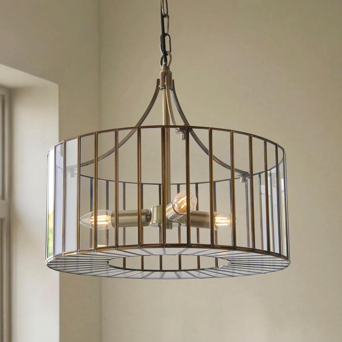 Antalya pendant's slatted brass drum shade lit by three candle bulbs against a green wall