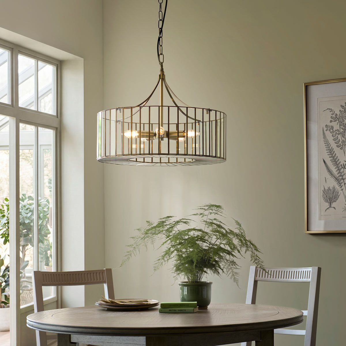 Antalya brass and clear glass pendant lit above a dining table with potted fern in a green room