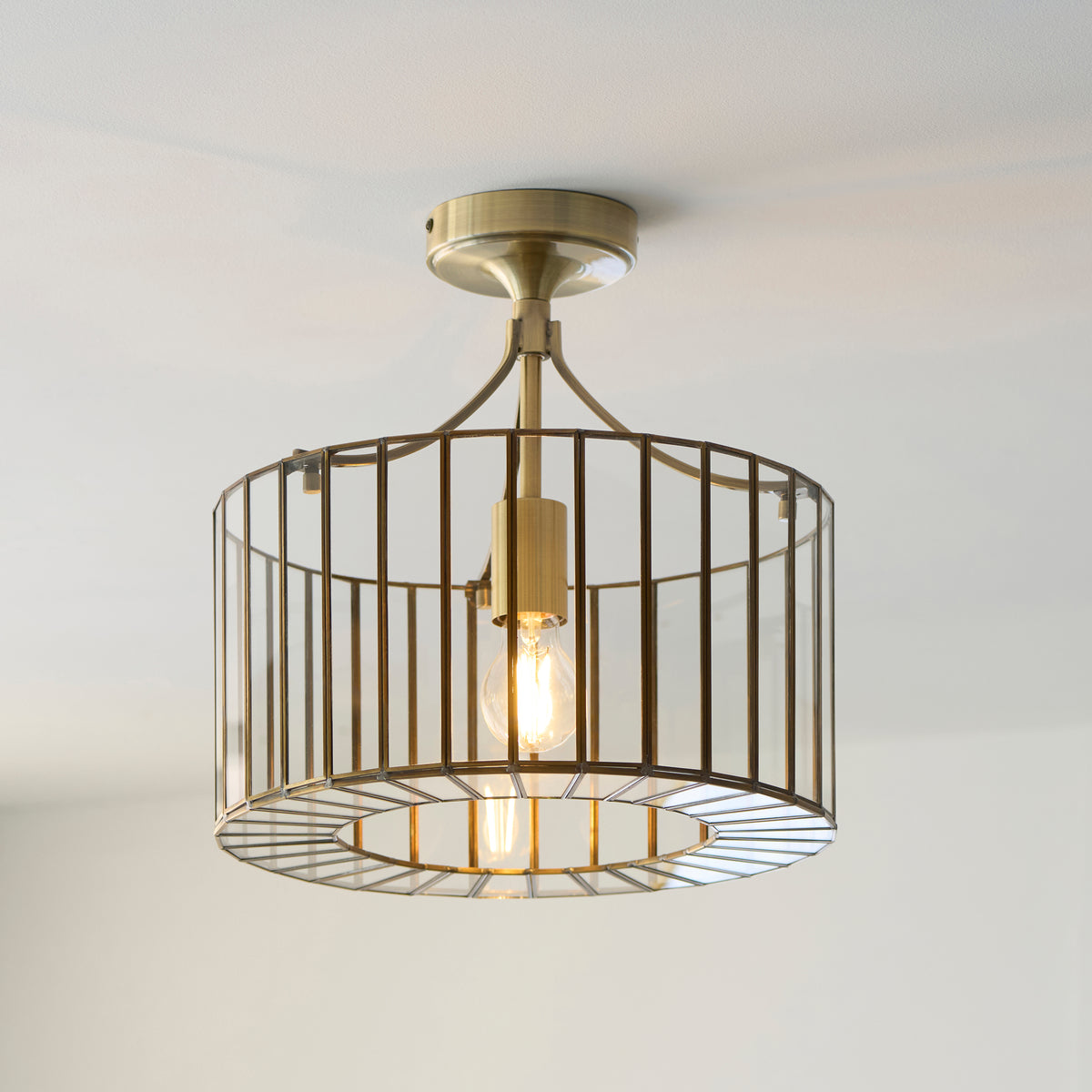 Antalya flush light lit on a white ceiling, its brass cage shade glowing softly