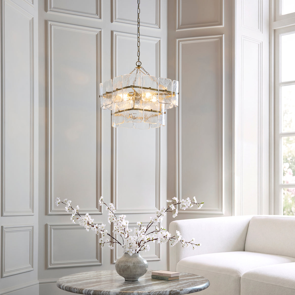 Venice aged brass and glass pendant lit in a panelled living room above a marble side table