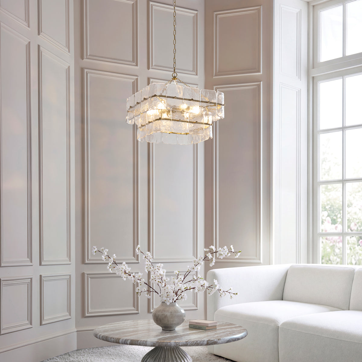 Venice brushed brass pendant lit above a marble table with blossom stems in a panelled room