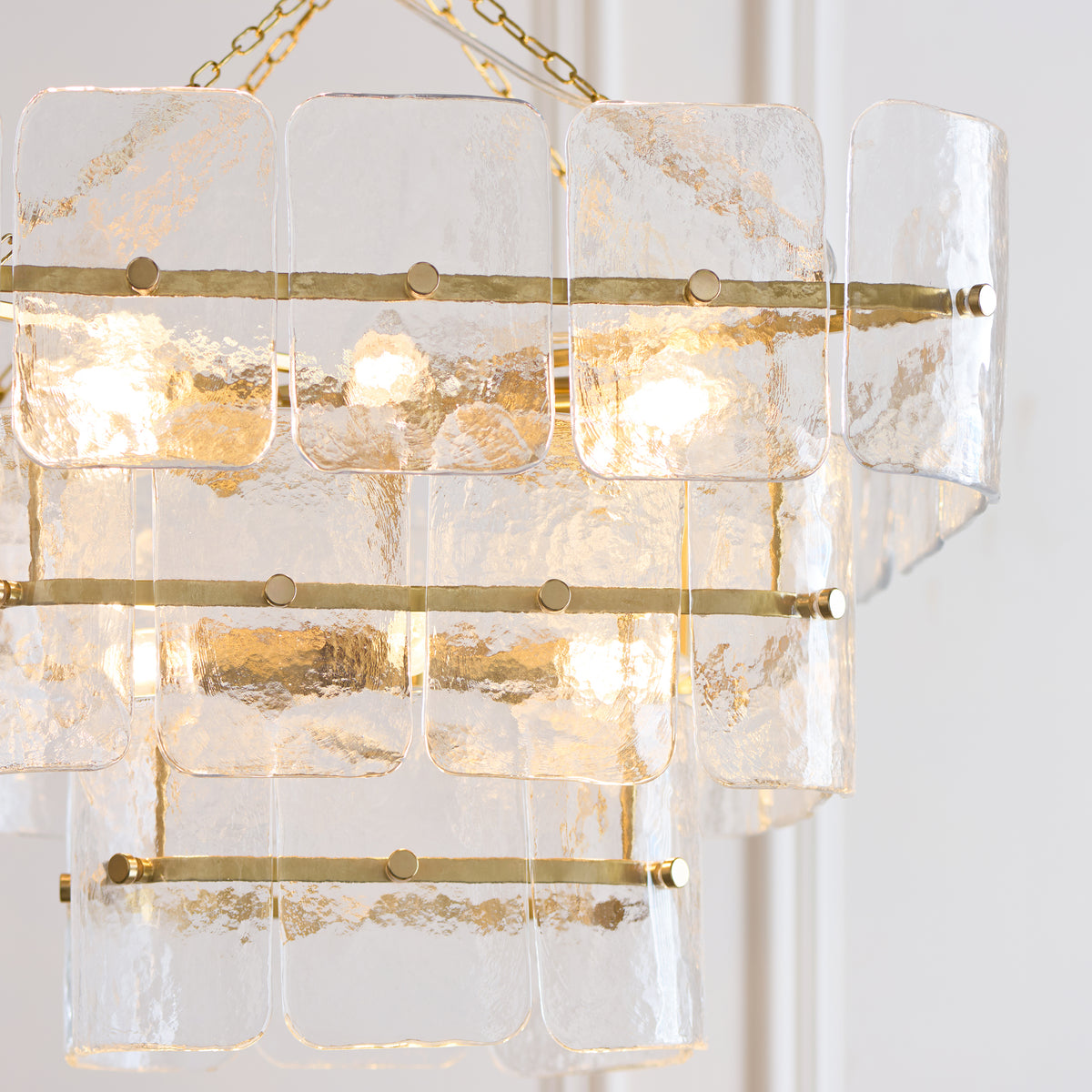 Close-up of the Venice chandelier's textured glass panels and brass rails with warm lamps behind