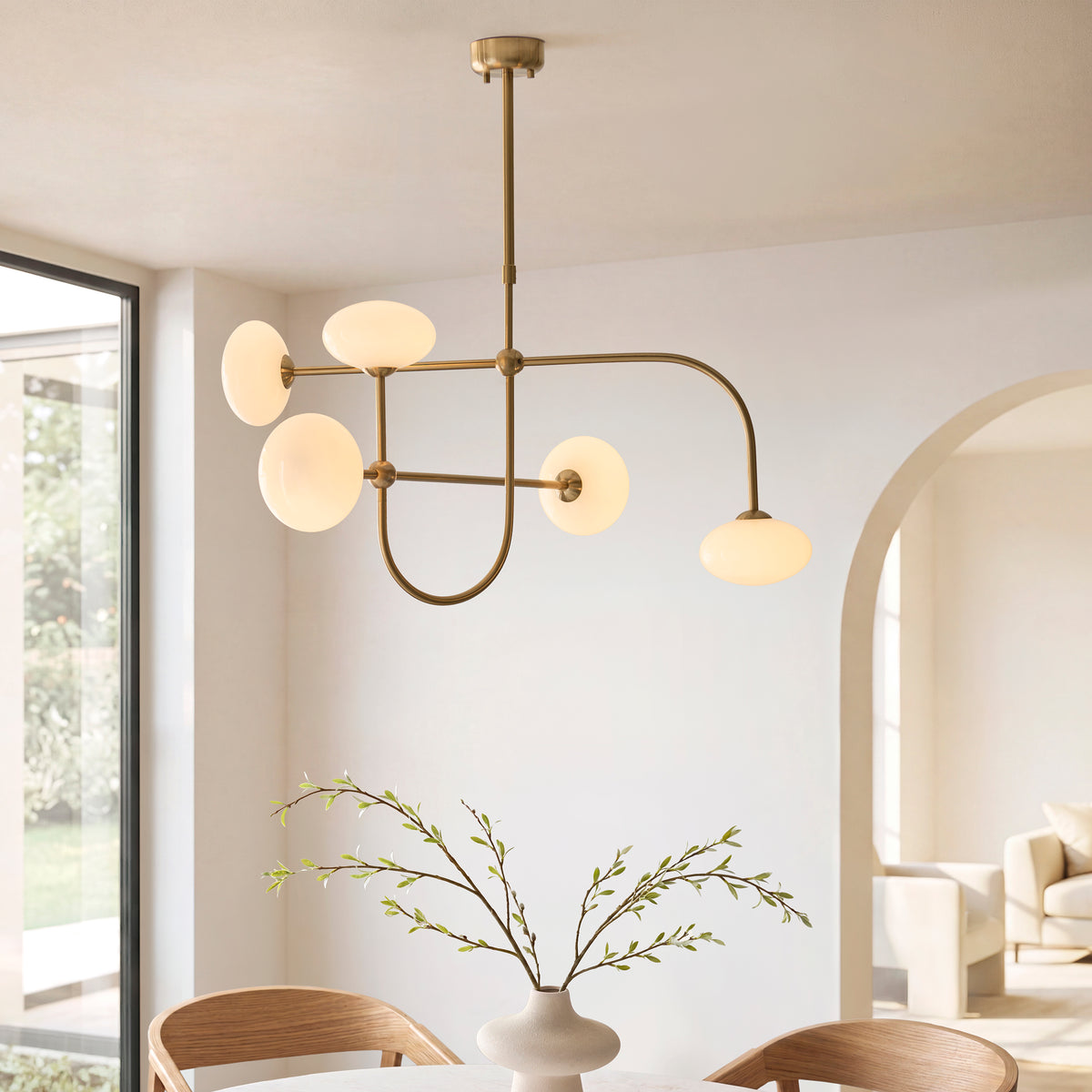 Ottowa brass and opal glass pendant lit above a wooden dining table beside tall windows