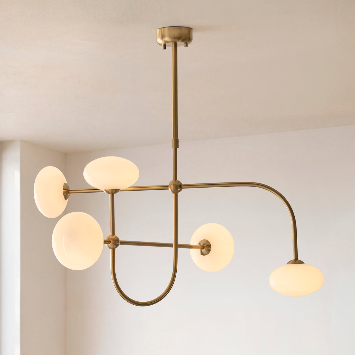 Ottowa pendant's brass arms and opal glass shades against a pale corner wall
