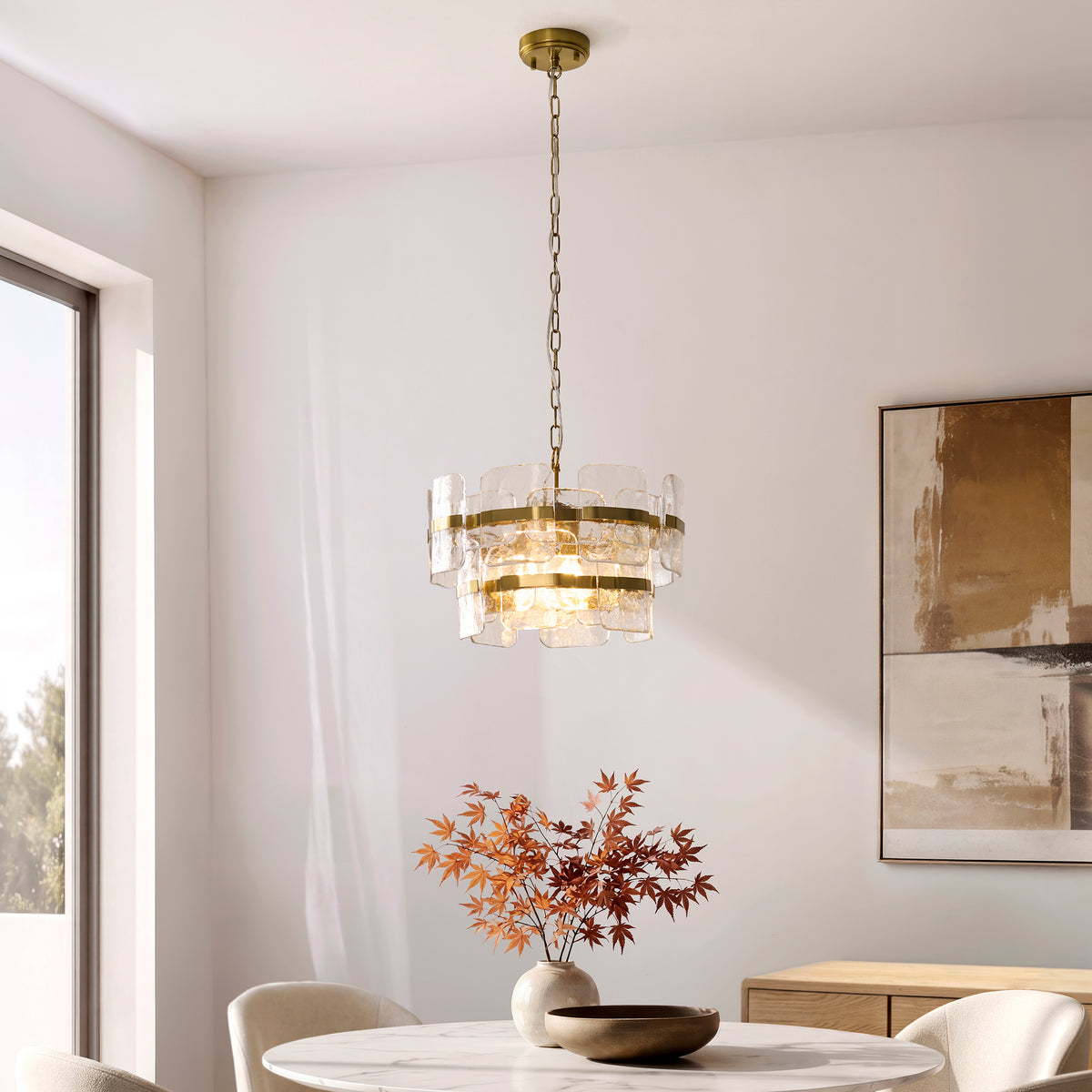 Ancara brass pendant lit above a round marble dining table with vase and abstract artwork