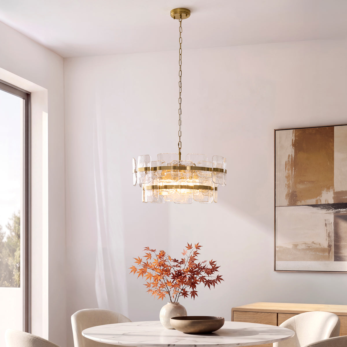Ancara chandelier lit above a marble dining table with artwork and autumn foliage nearby