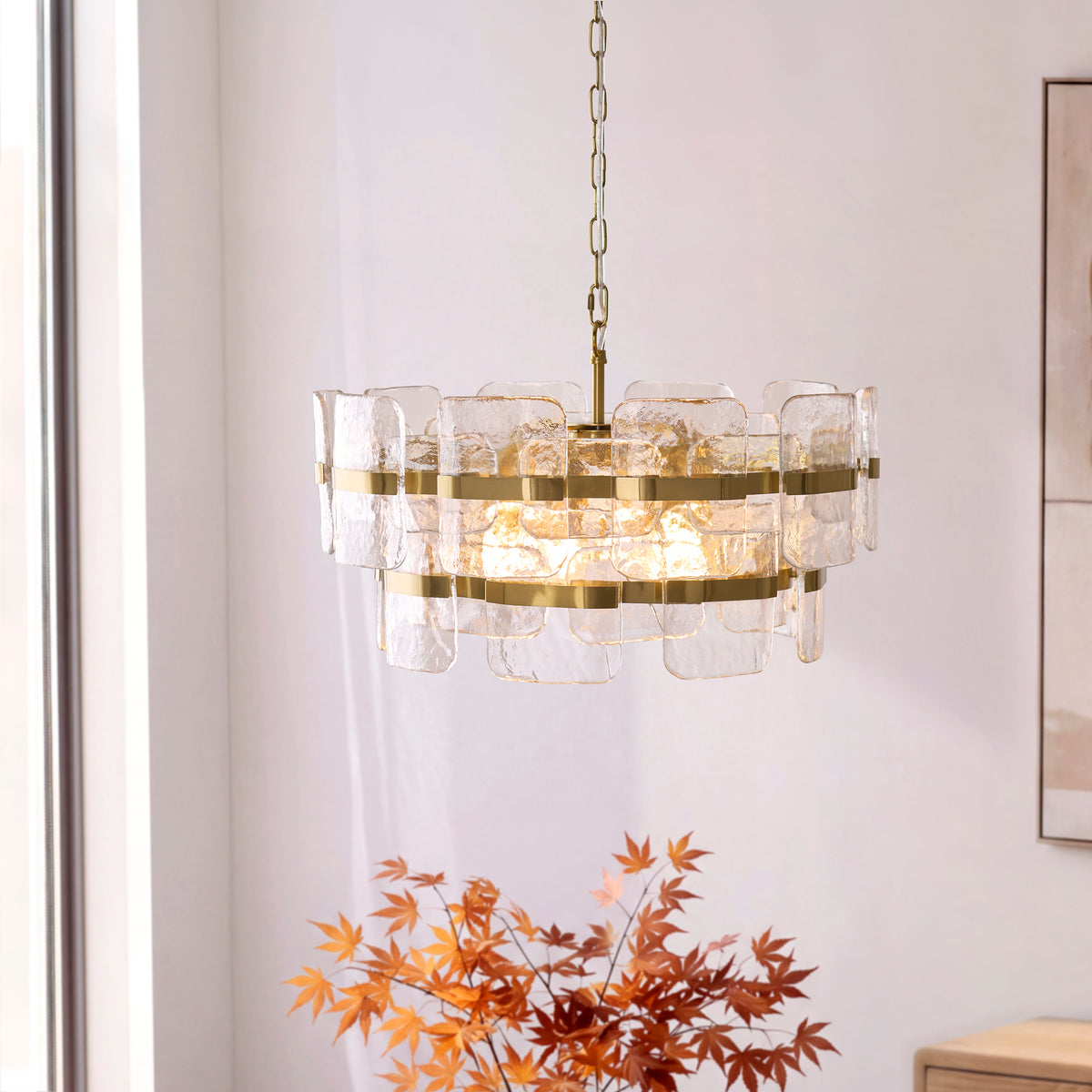 Ancara aged brass chandelier glowing warmly on a pale wall beside framed artwork