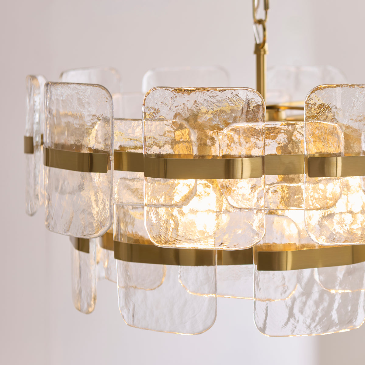 Angled detail of the Ancara chandelier's overlapping glass panels and gleaming brass rings