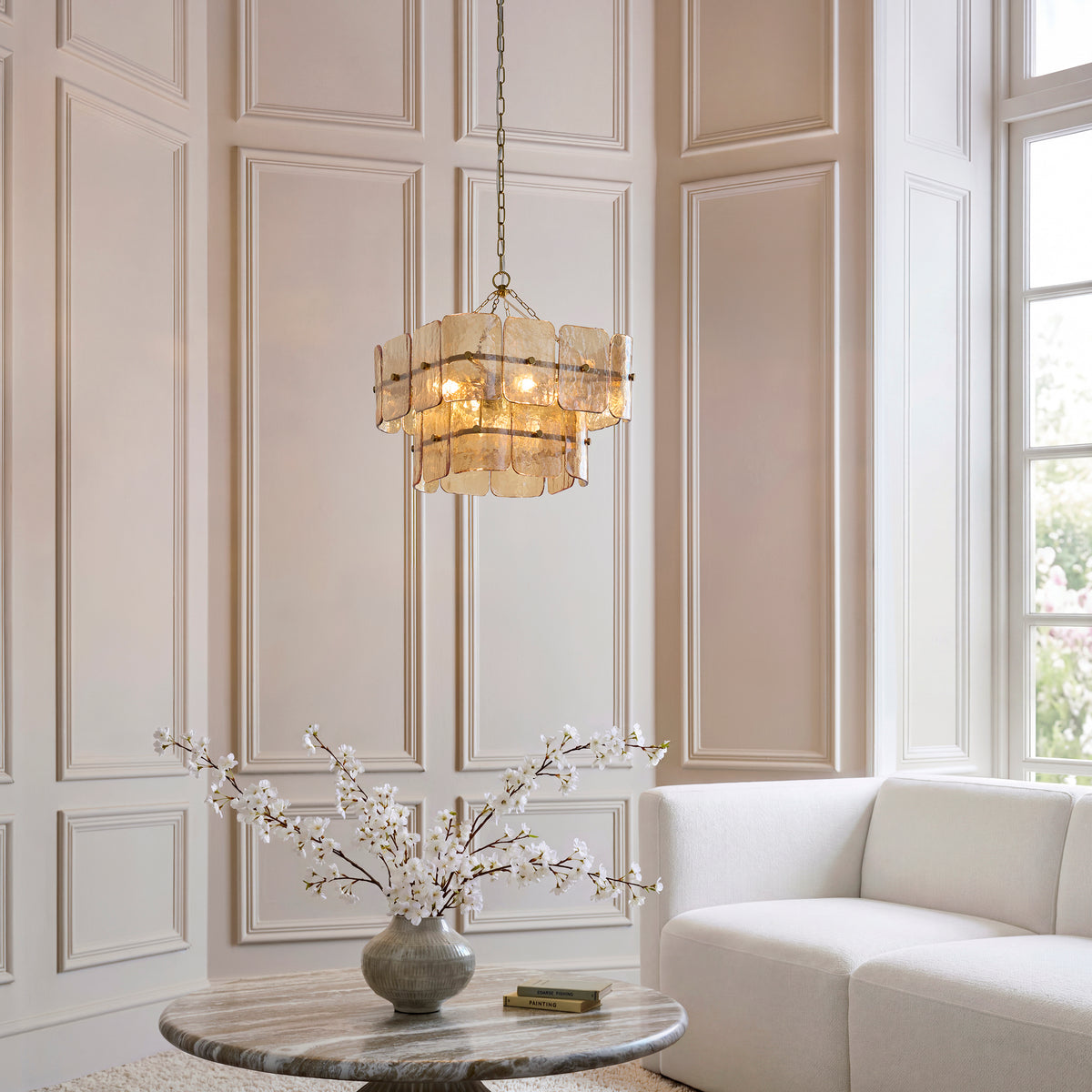 Venice chandelier lit above a marble table and cream sofa in a tall panelled living room