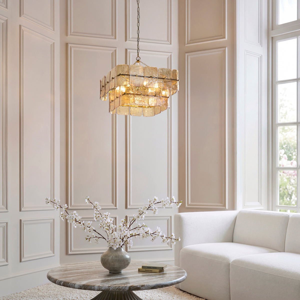 Venice champagne chandelier lit above a marble table and cream sofa in a panelled room