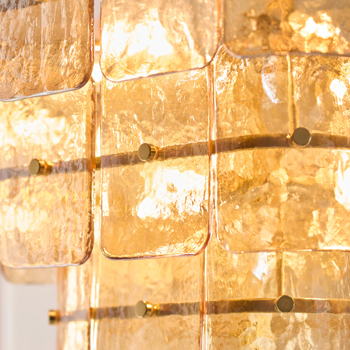 Detail of glowing textured champagne glass panels held by brass studs on the Venice pendant