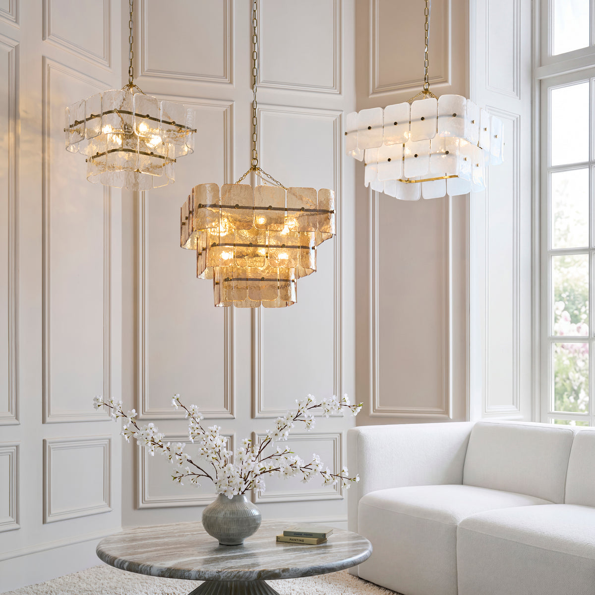 Three Venice chandeliers in white, champagne and clear glass over a marble table in a panelled room