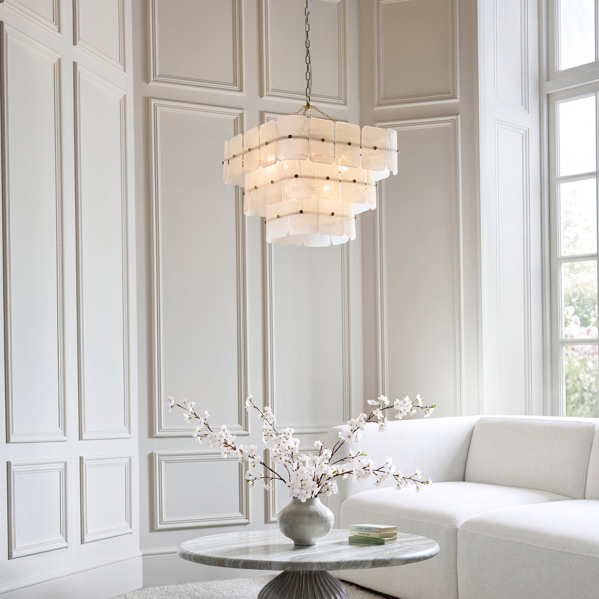 Venice 10 light chandelier lit in a bright panelled living room above a marble table and cream sofa