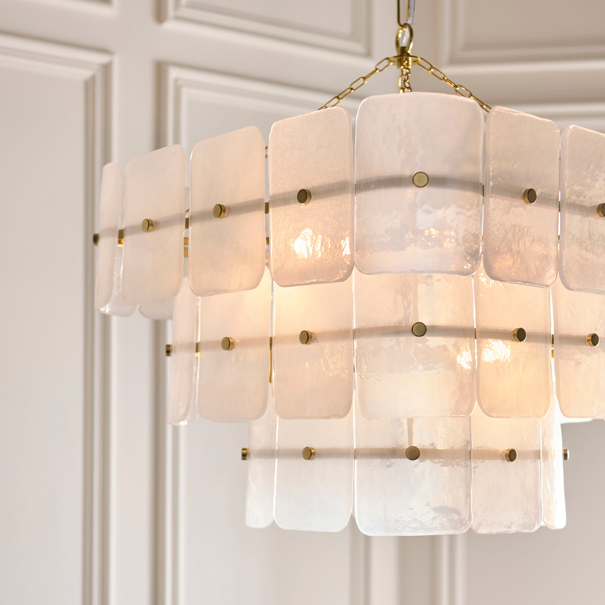 Venice 10 light chandelier lit from within, brass studs securing layered white textured glass panels