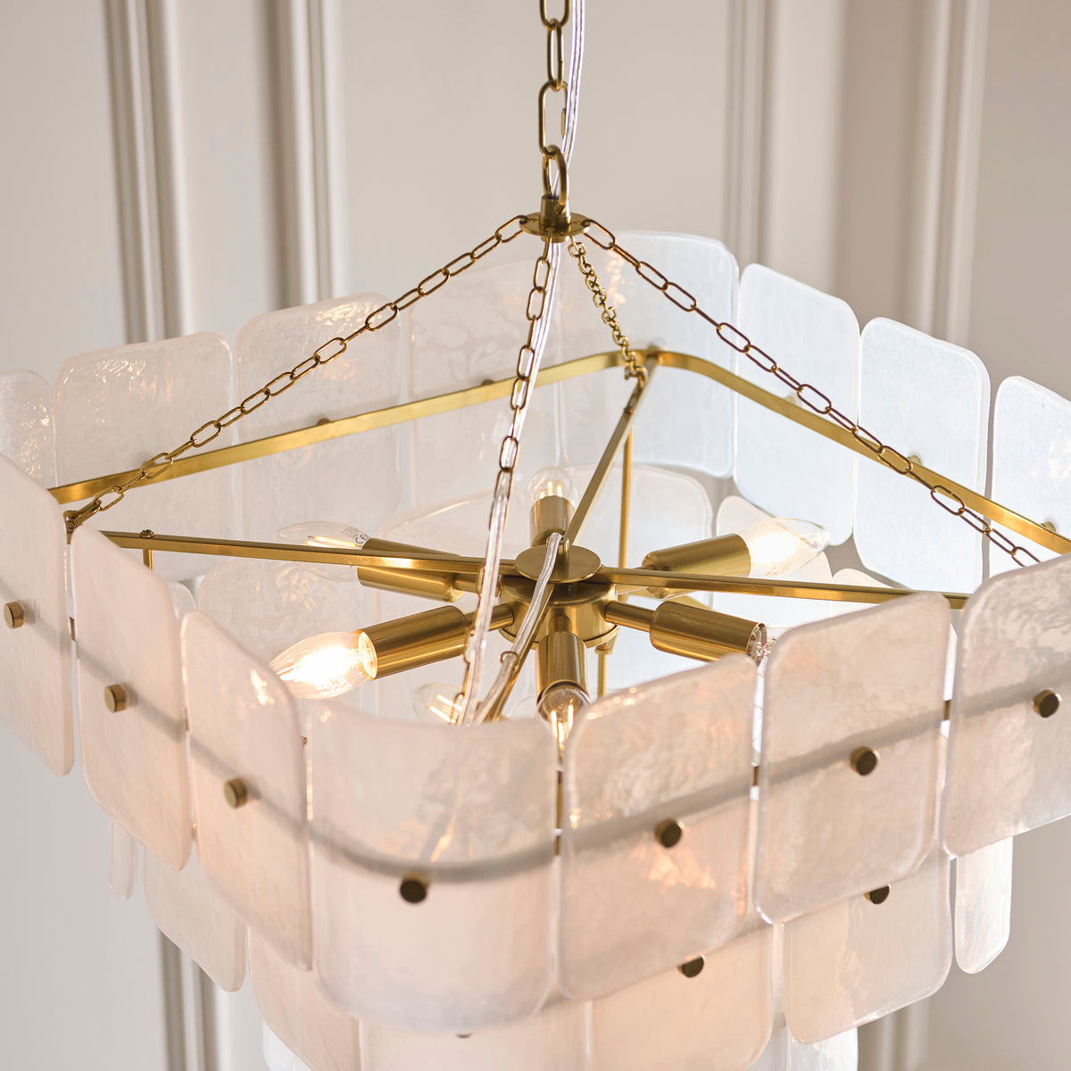 Underside of the Venice 10 light chandelier with brass hub, lit lamps and square glass panel frame