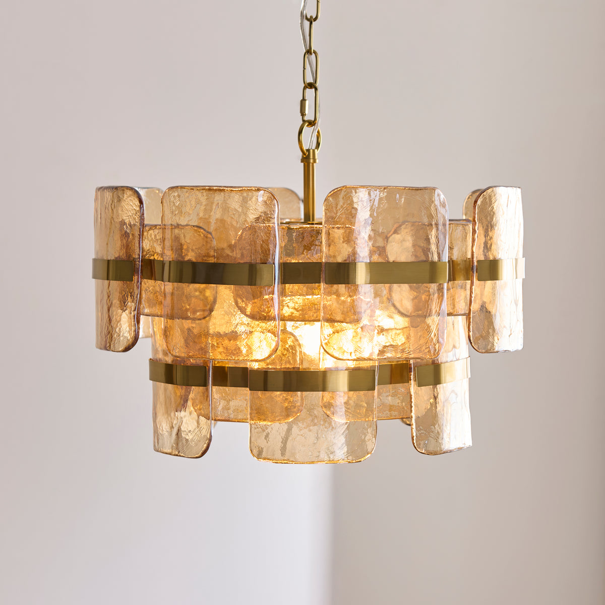 Ancara pendant glowing warmly, its champagne glass panels held by wide brushed brass bands