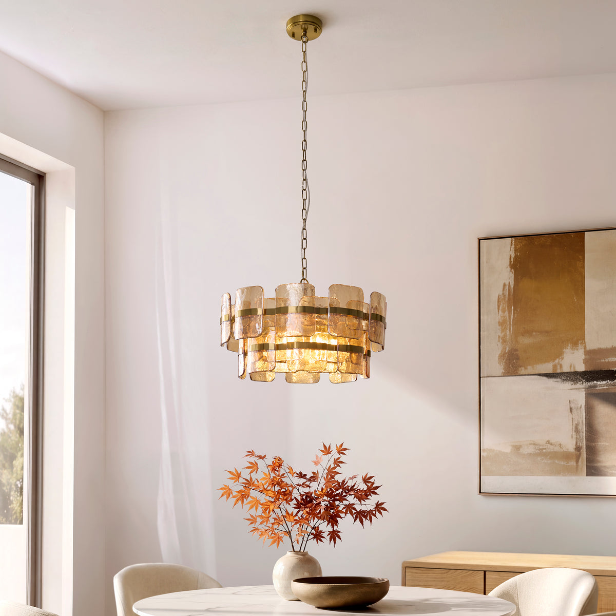 Ancara 6 light pendant lit above a dining table with autumn branches and abstract artwork behind
