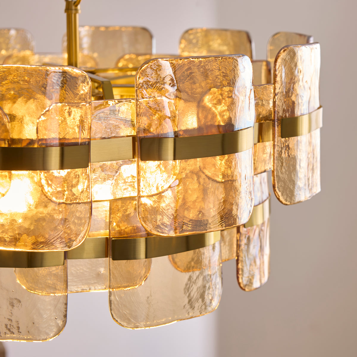 Close view of the Ancara pendant's champagne textured glass panels held by broad brushed brass bands