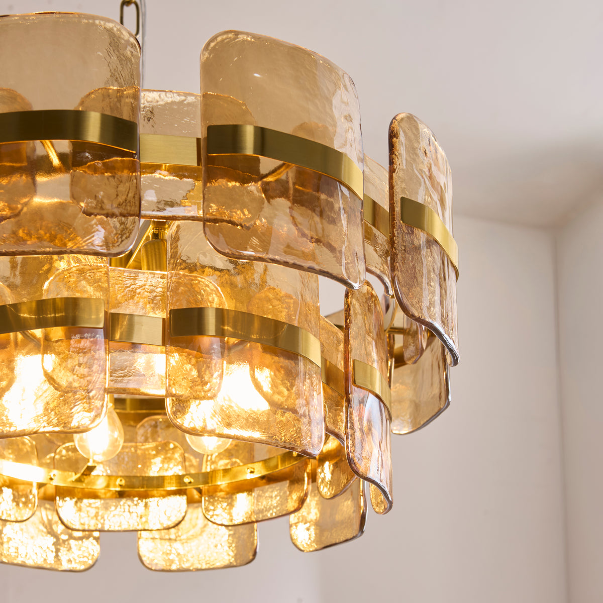Angled detail of the Ancara pendant showing lit lamps behind tiers of amber-toned textured glass