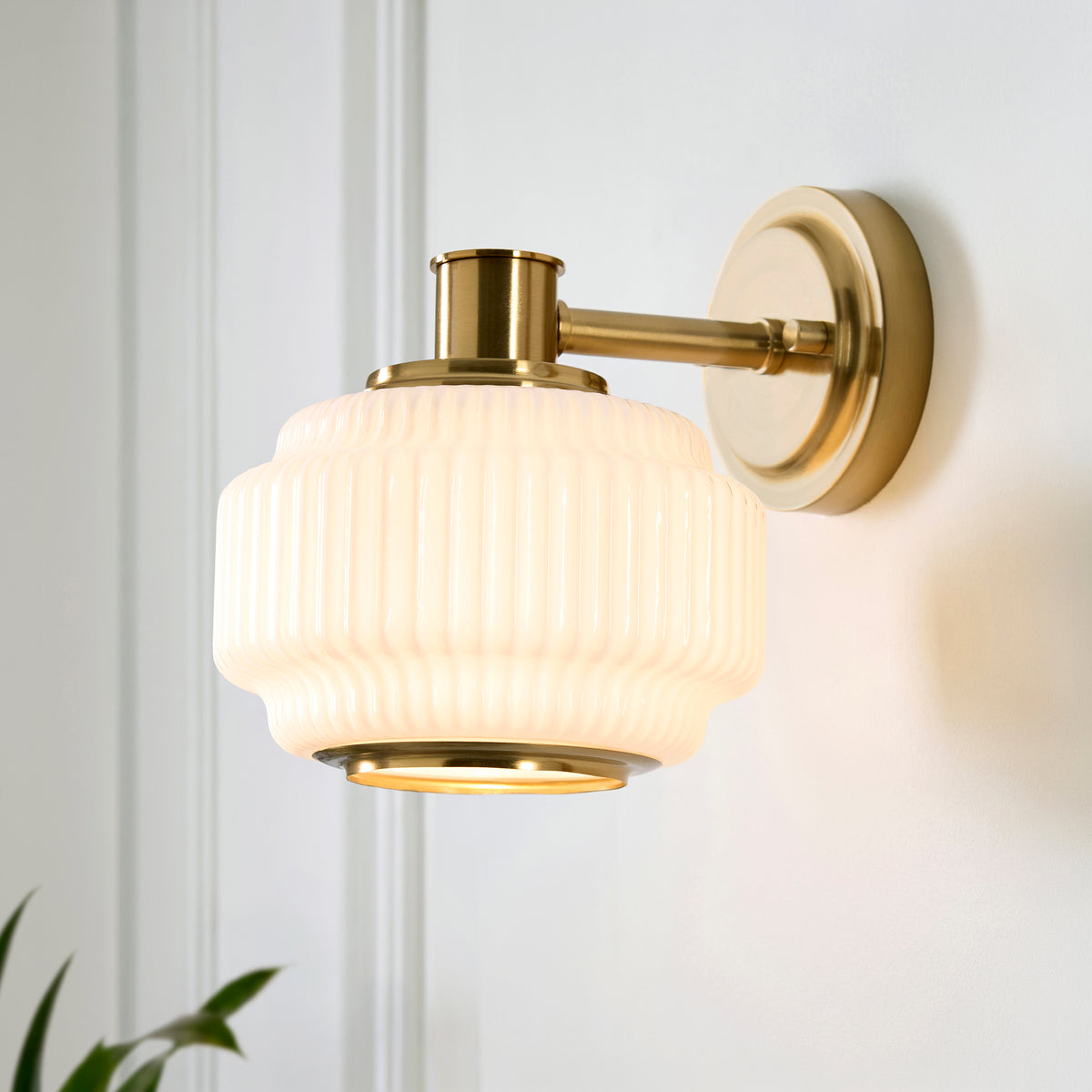 Evora wall light on a panelled wall, its ribbed opal glass shade set on a brushed brass arm