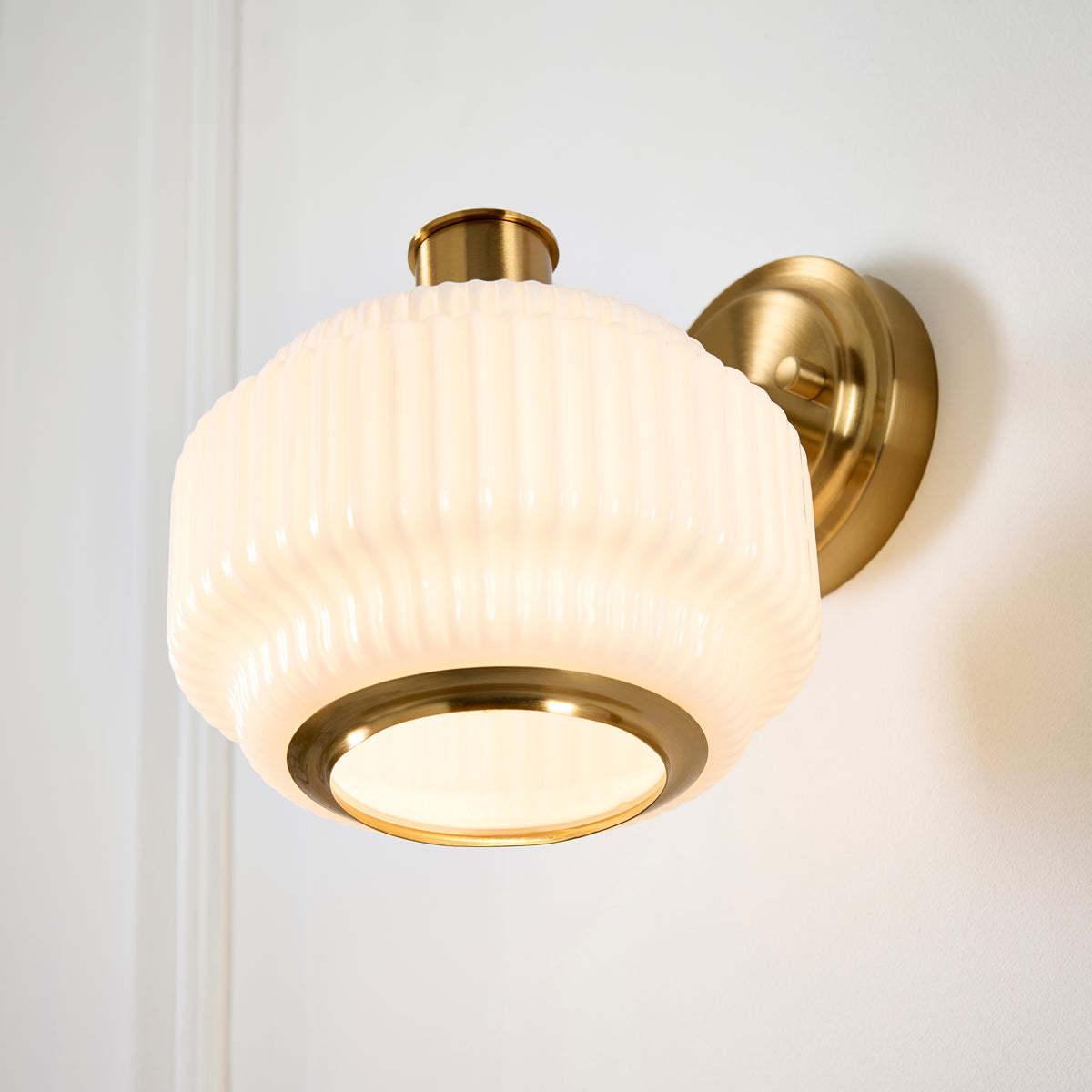 Evora wall light lit against panelling, warm glow spilling from the ribbed opal glass shade