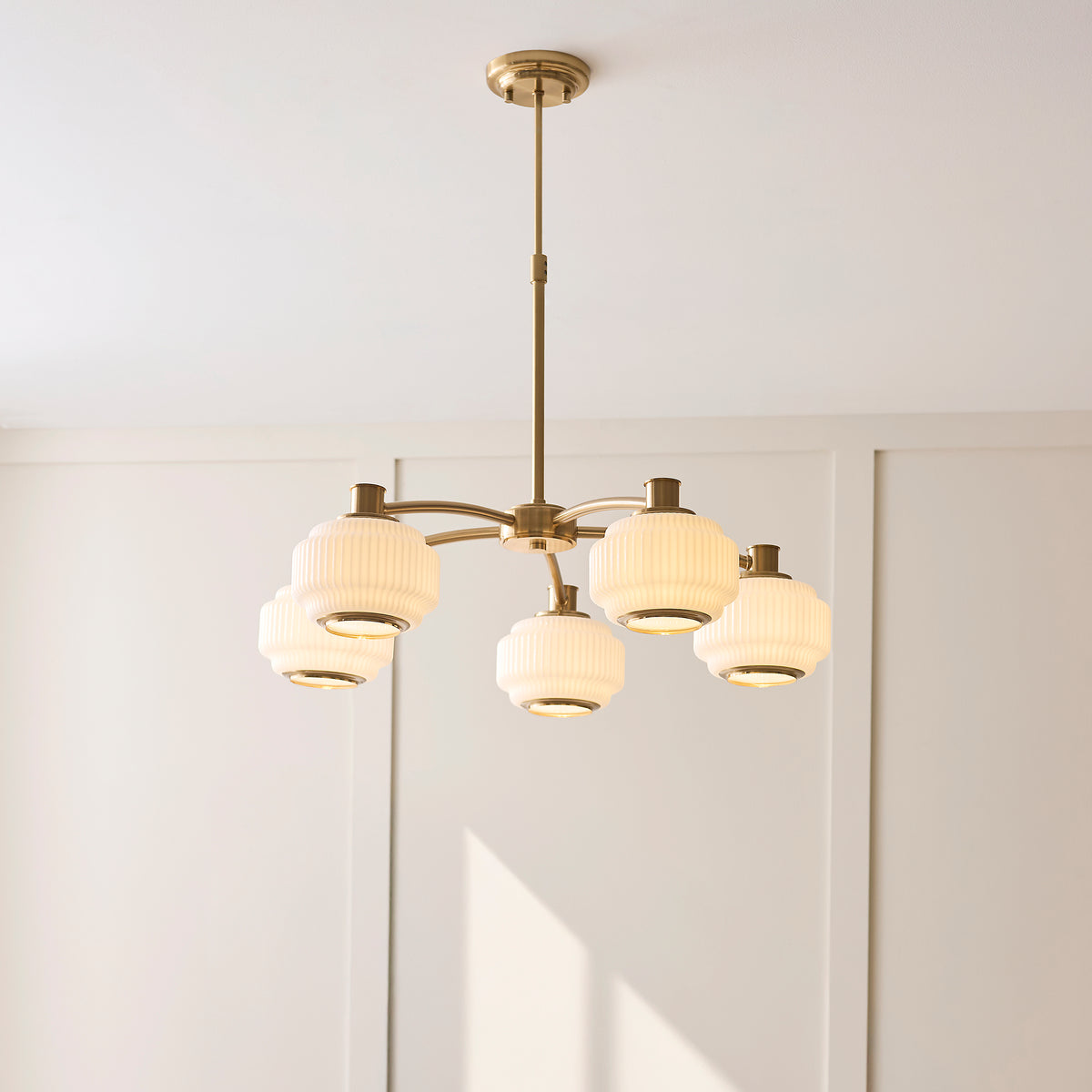 Evora 5 light chandelier lit in a panelled room, ribbed opal shades glowing on brass arms