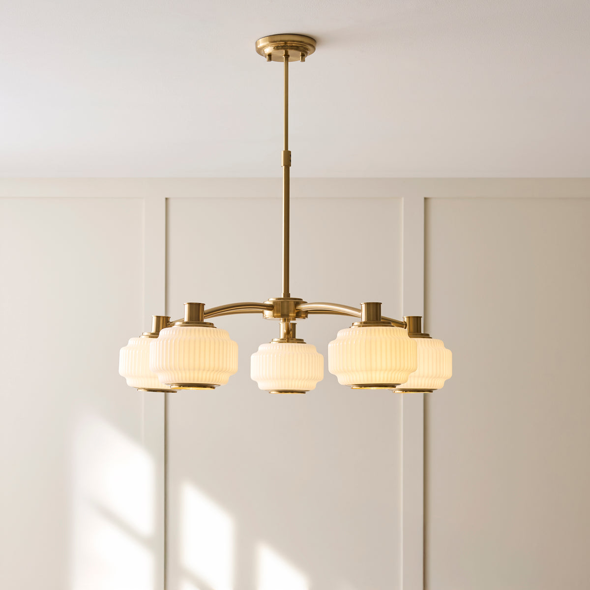 Evora brass chandelier with five ribbed opal glass shades hung in a sunlit panelled interior
