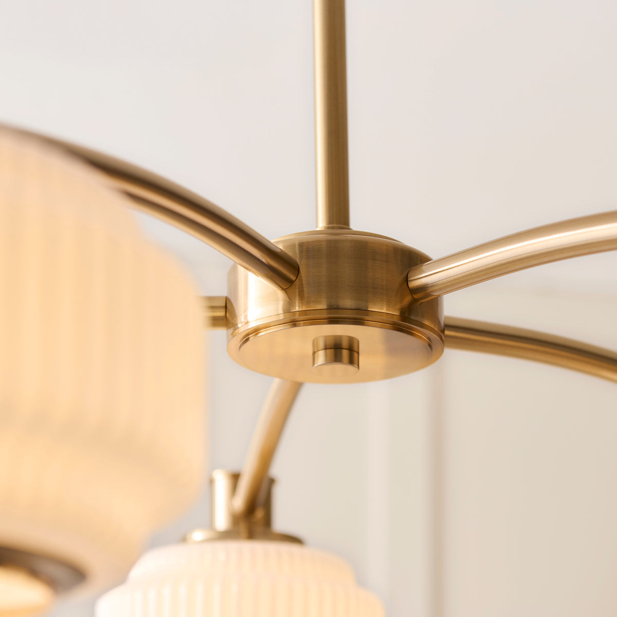 Detail of the Evora chandelier's brushed brass hub and curved arms holding opal glass shades