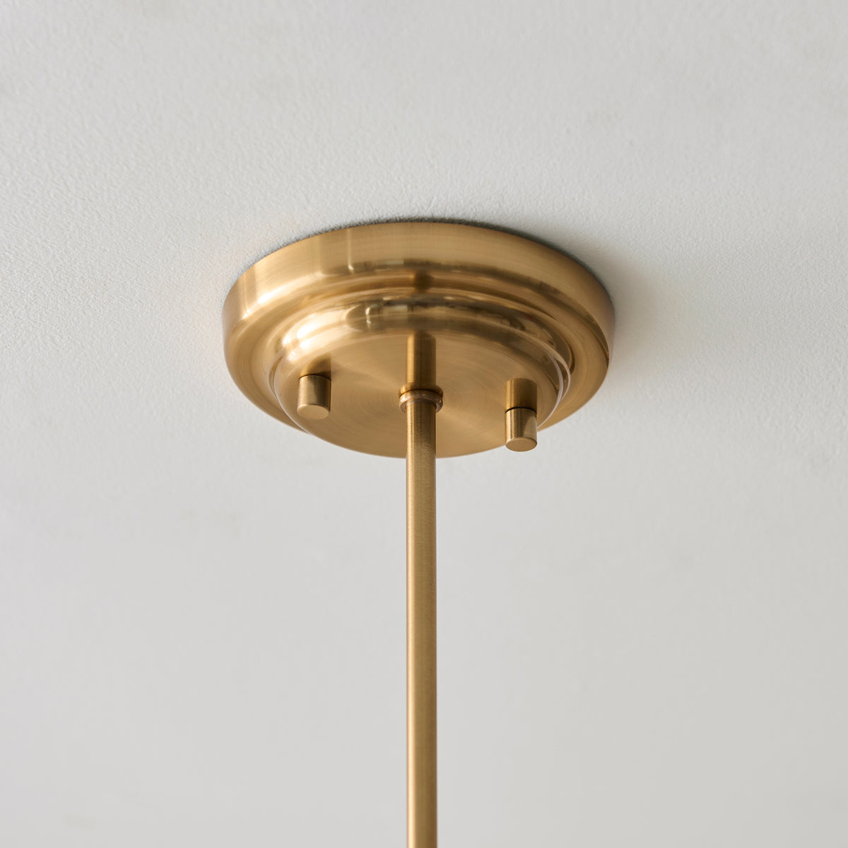 Brushed brass ceiling plate and drop rod of the Evora chandelier fitted to a white ceiling