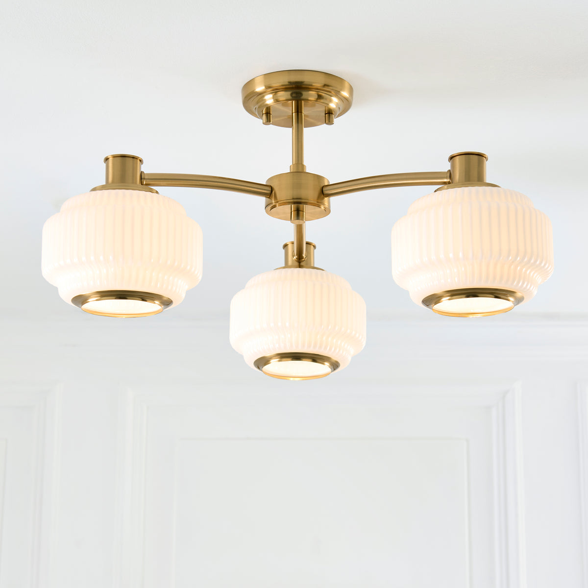 Evora brass semi flush light against white panelling, its three ribbed opal shades glowing