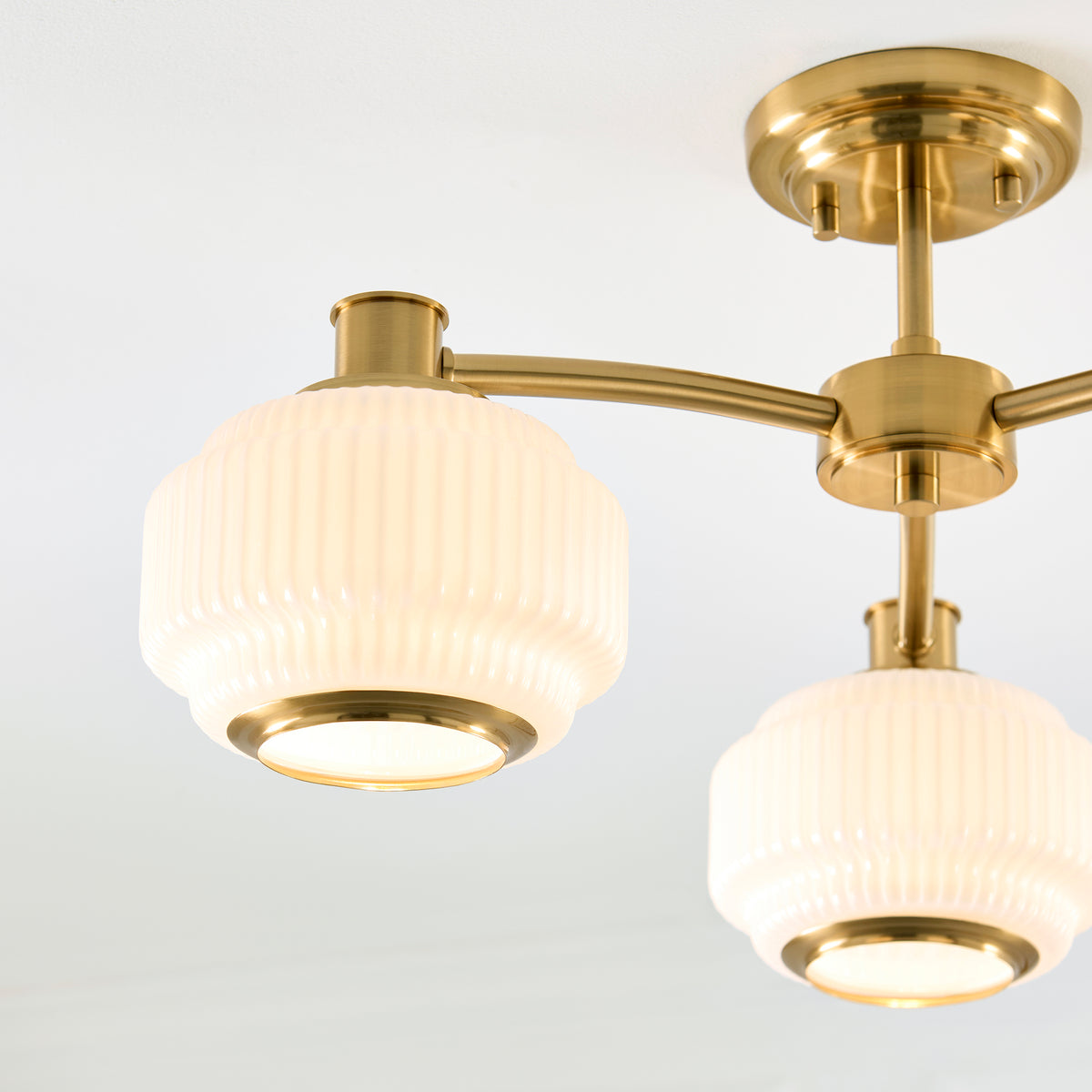 Angled close view of the Evora semi flush light's ribbed opal shades and brushed brass arms