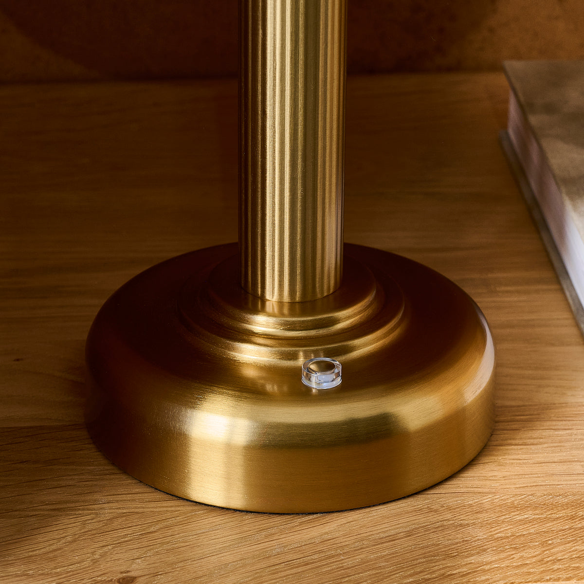 Close-up of the Bridport table lamp's warm brass fluted stem and stepped base with touch dimmer switch