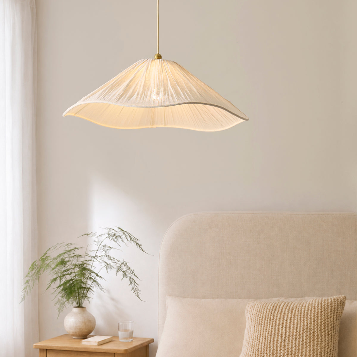 Isabella Grand pendant lit above a bedroom, with upholstered headboard, cushions and plant on bedside table
