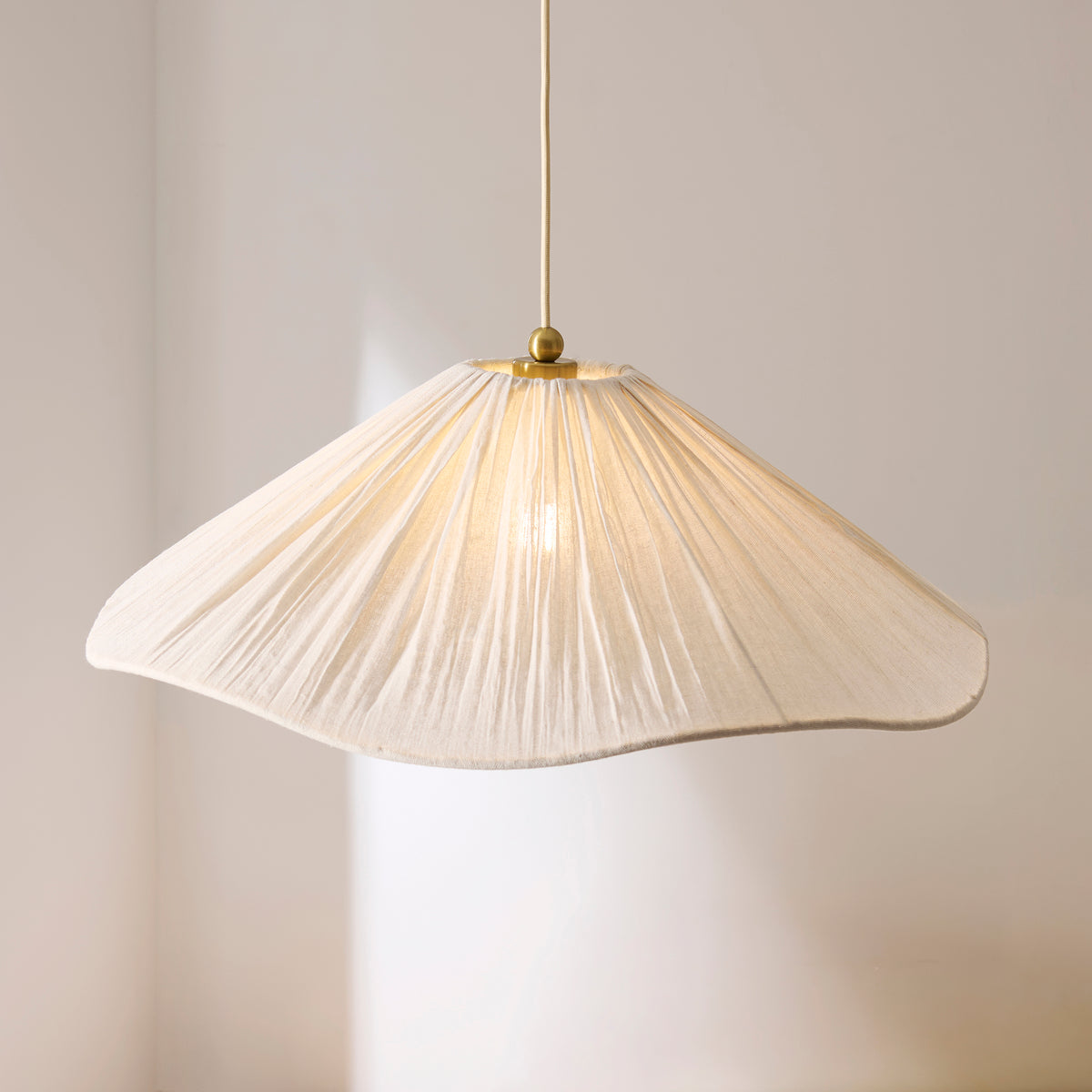 Isabella Grand pendant's pleated cream scalloped shade glowing softly against a pale wall