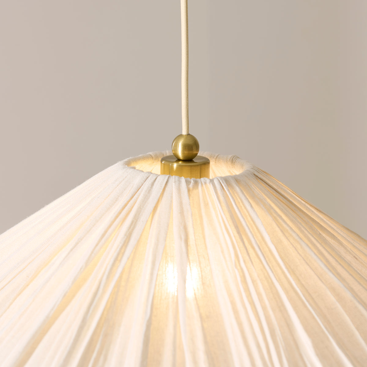 Detail of the Isabella Grand pendant's brass ball finial and gathered pleats with lit bulb visible