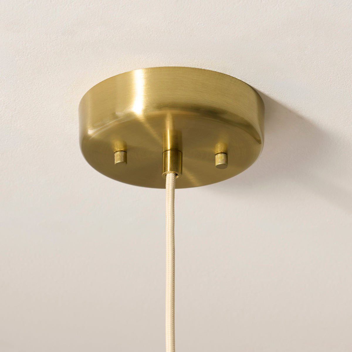 Aged brass ceiling rose of the Isabella Grand pendant with ivory braided flex against a white ceiling