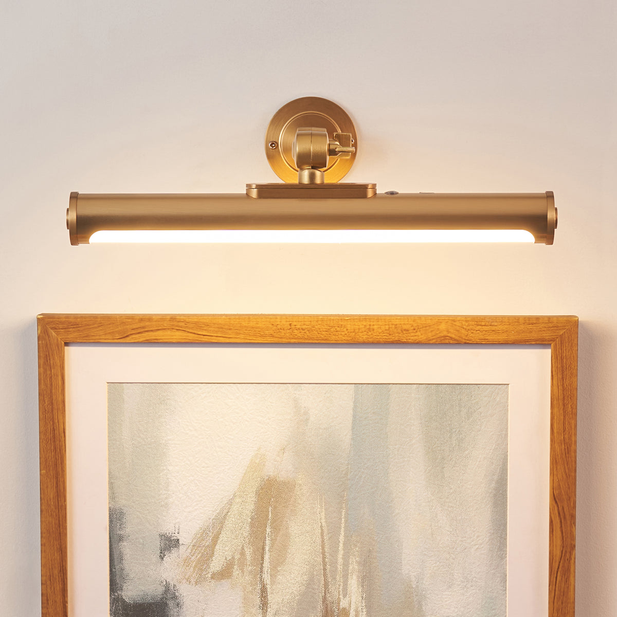 Kas warm brass picture light lit above an oak-framed abstract artwork on a panelled wall
