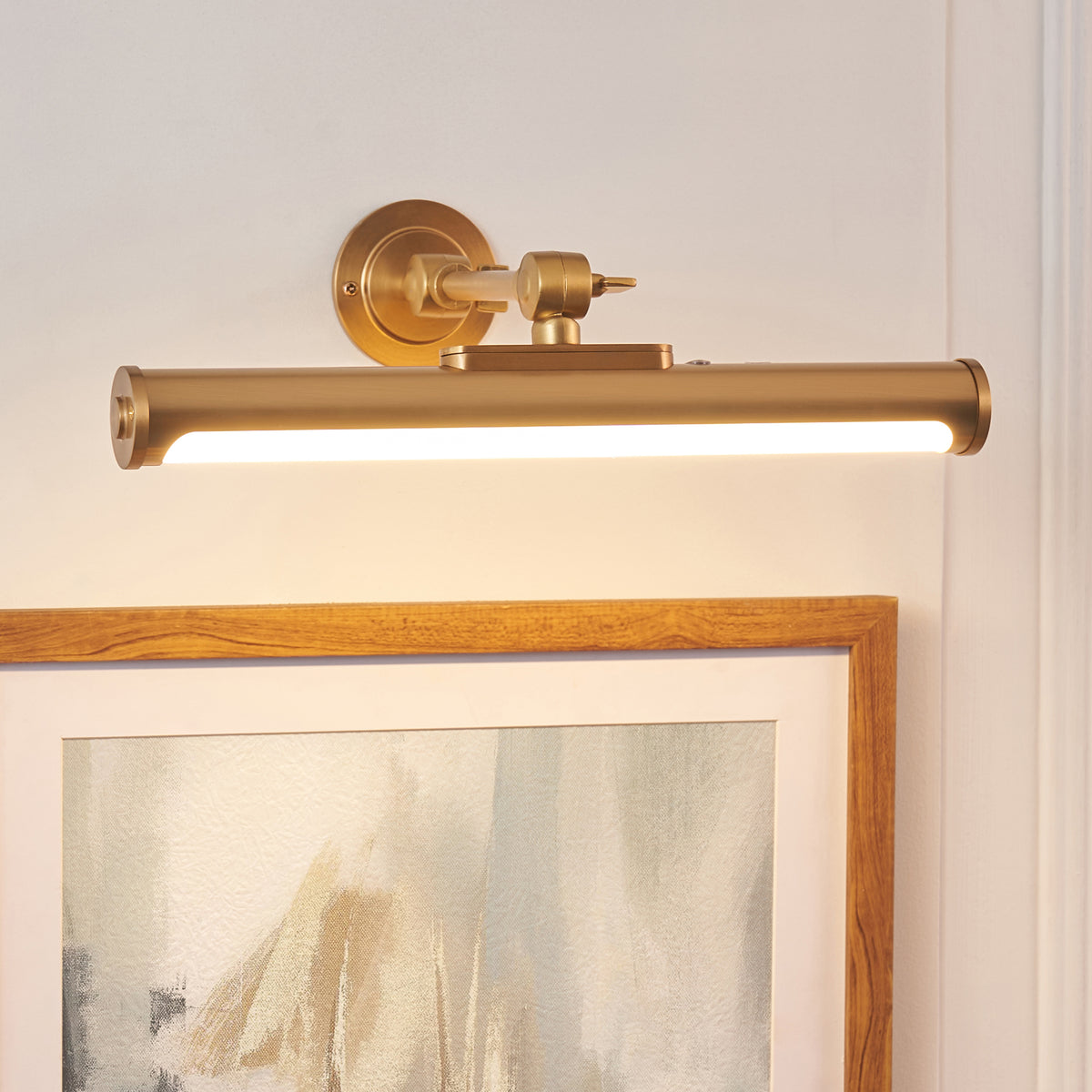 Angled view of the Kas picture light's brass tube casting warm light over a framed print