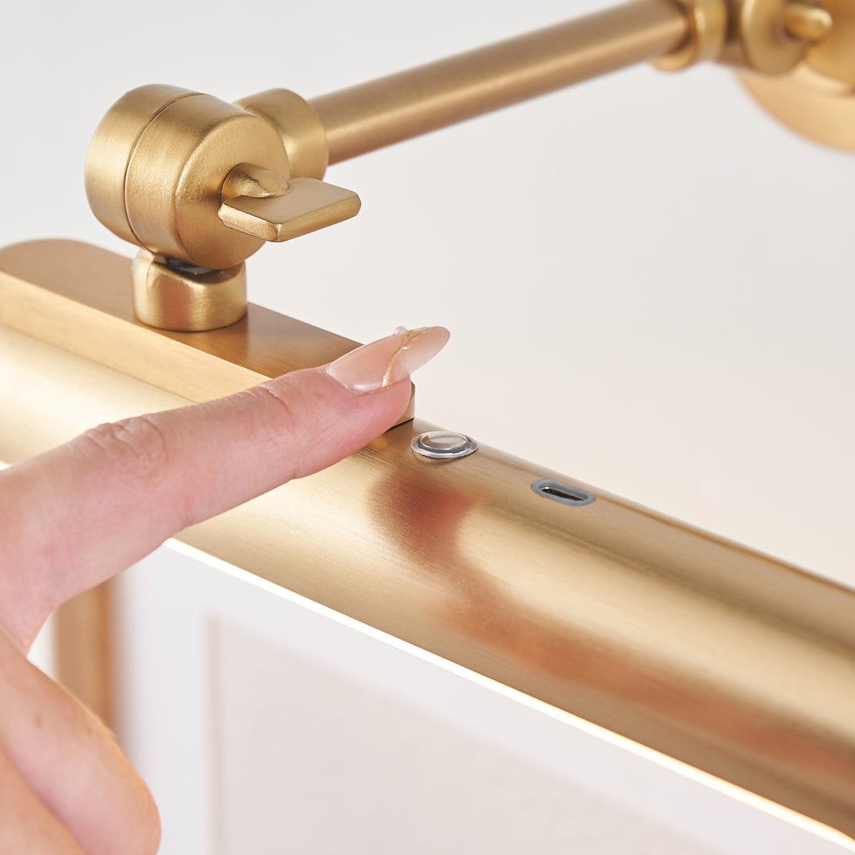 Finger pressing the touch button and USB-C port on the Kas brass picture light's tube