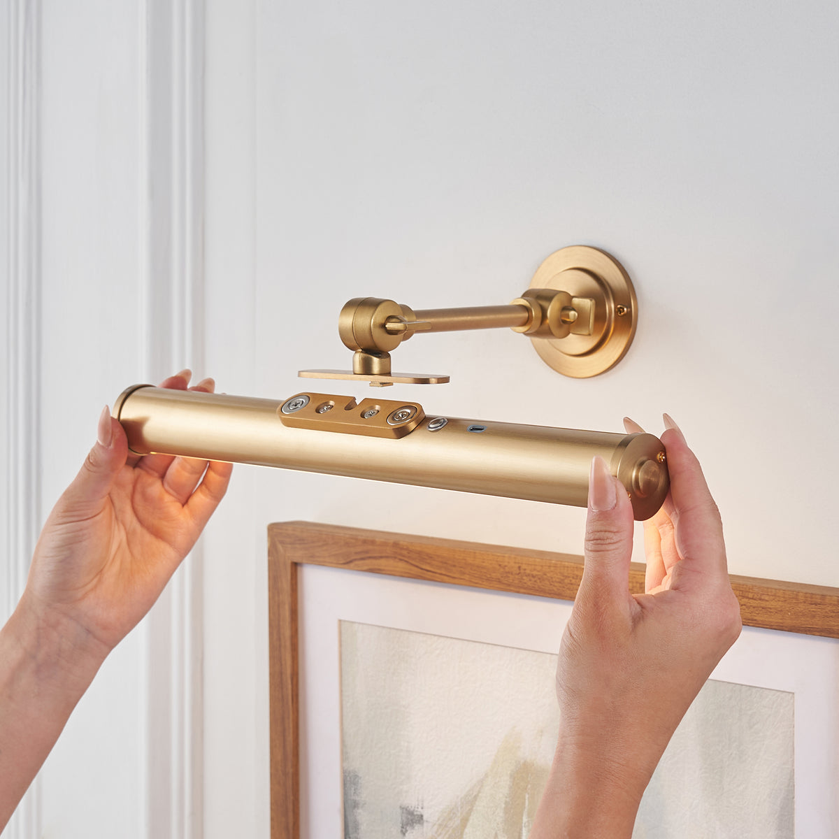 Hands lifting the Kas picture light body off its magnetic brass wall bracket for recharging