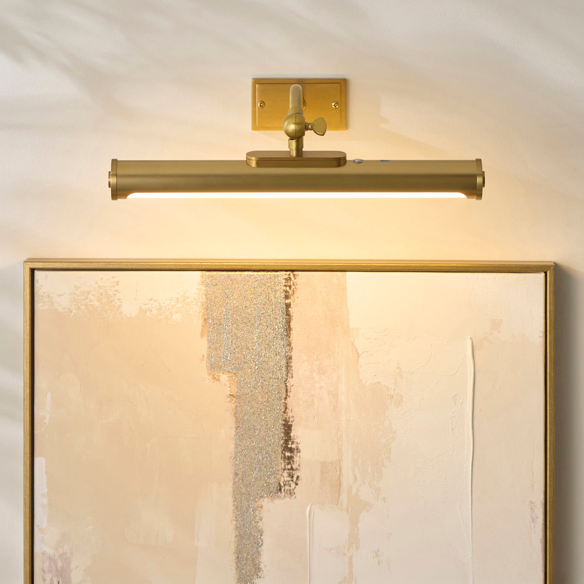 Maris brass picture light lit above a gold-framed abstract canvas on a white panelled wall