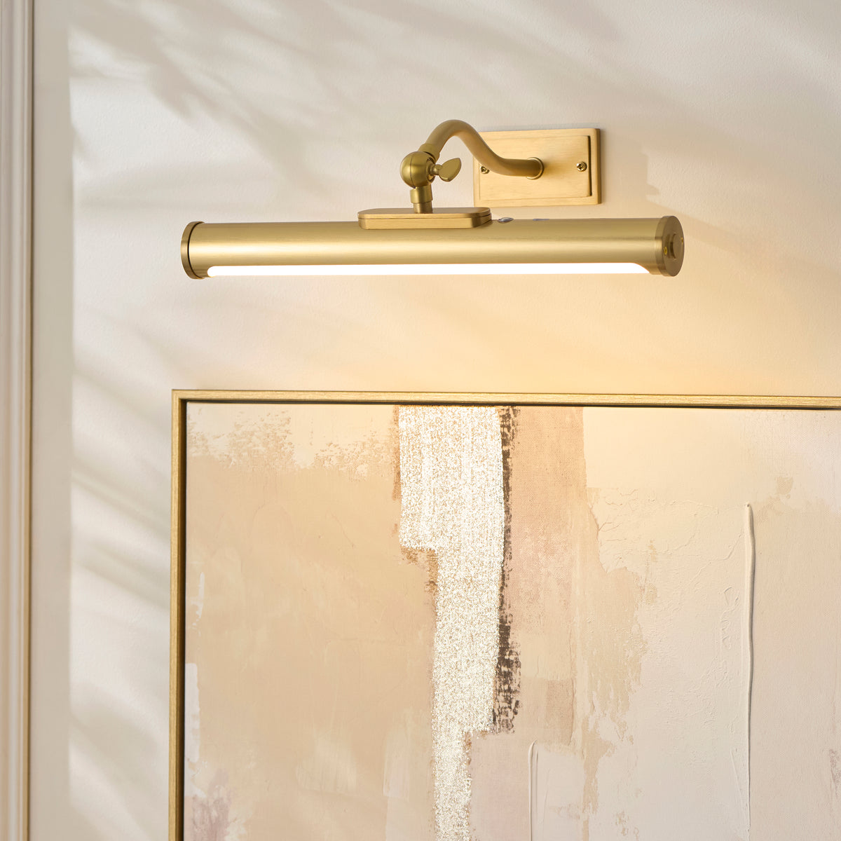 Maris warm brass picture light casting soft light across a gold-framed textured abstract painting