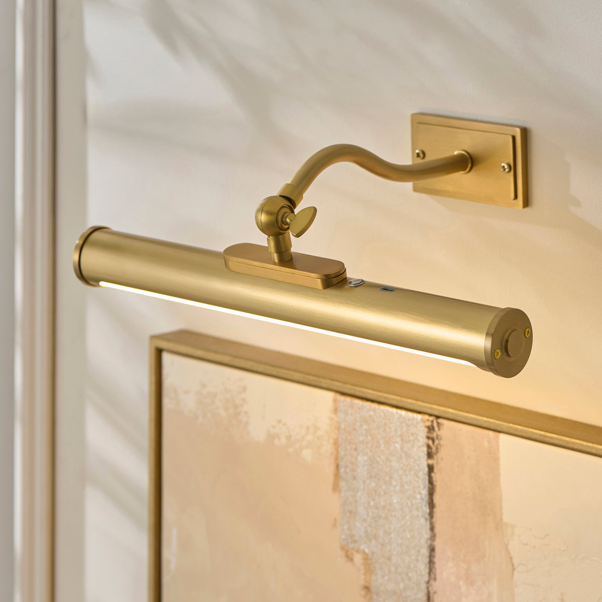 Close-up of the Maris picture light's brass tube, thumbscrew tilt joint and curved arm above a frame