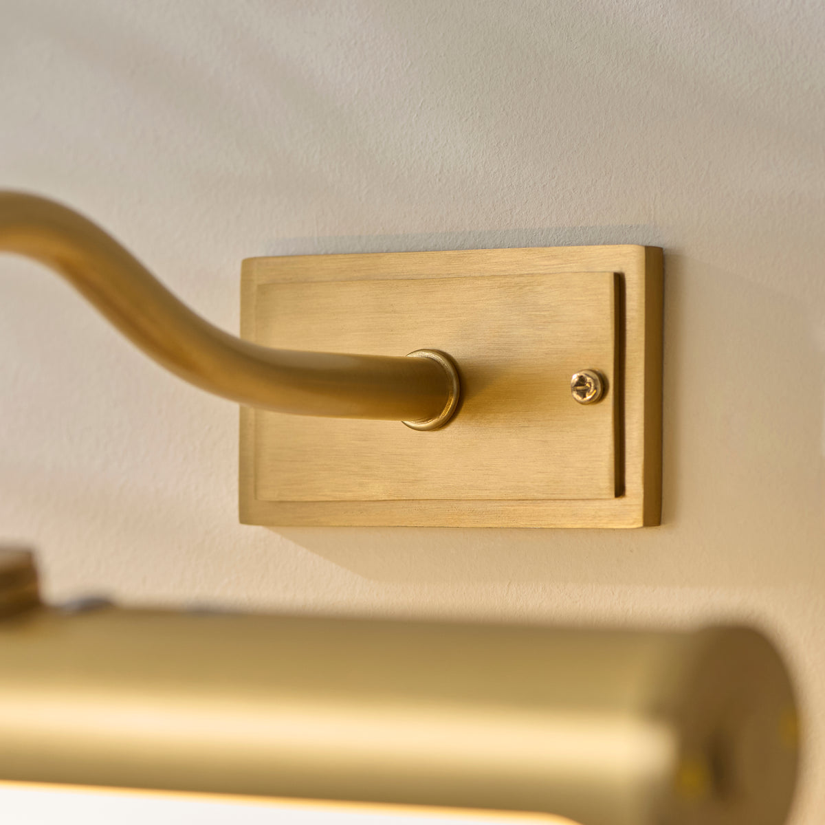 Close-up of the Maris picture light's rectangular brushed brass wall plate and curved brass arm