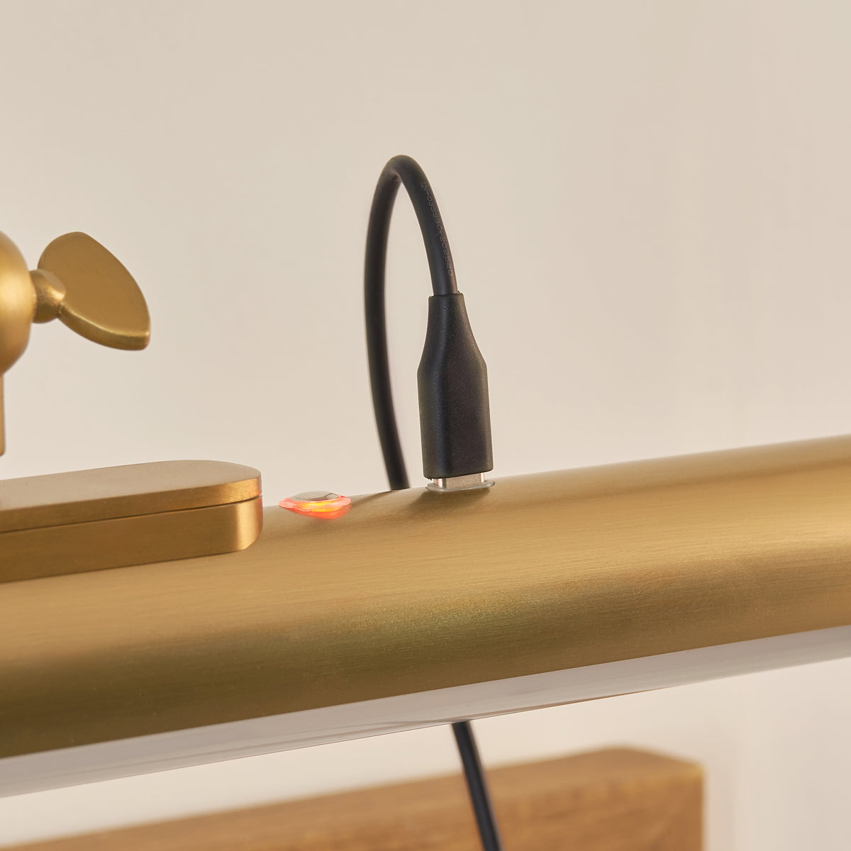 Charging cable plugged into the Maris brass picture light tube with the charge indicator glowing