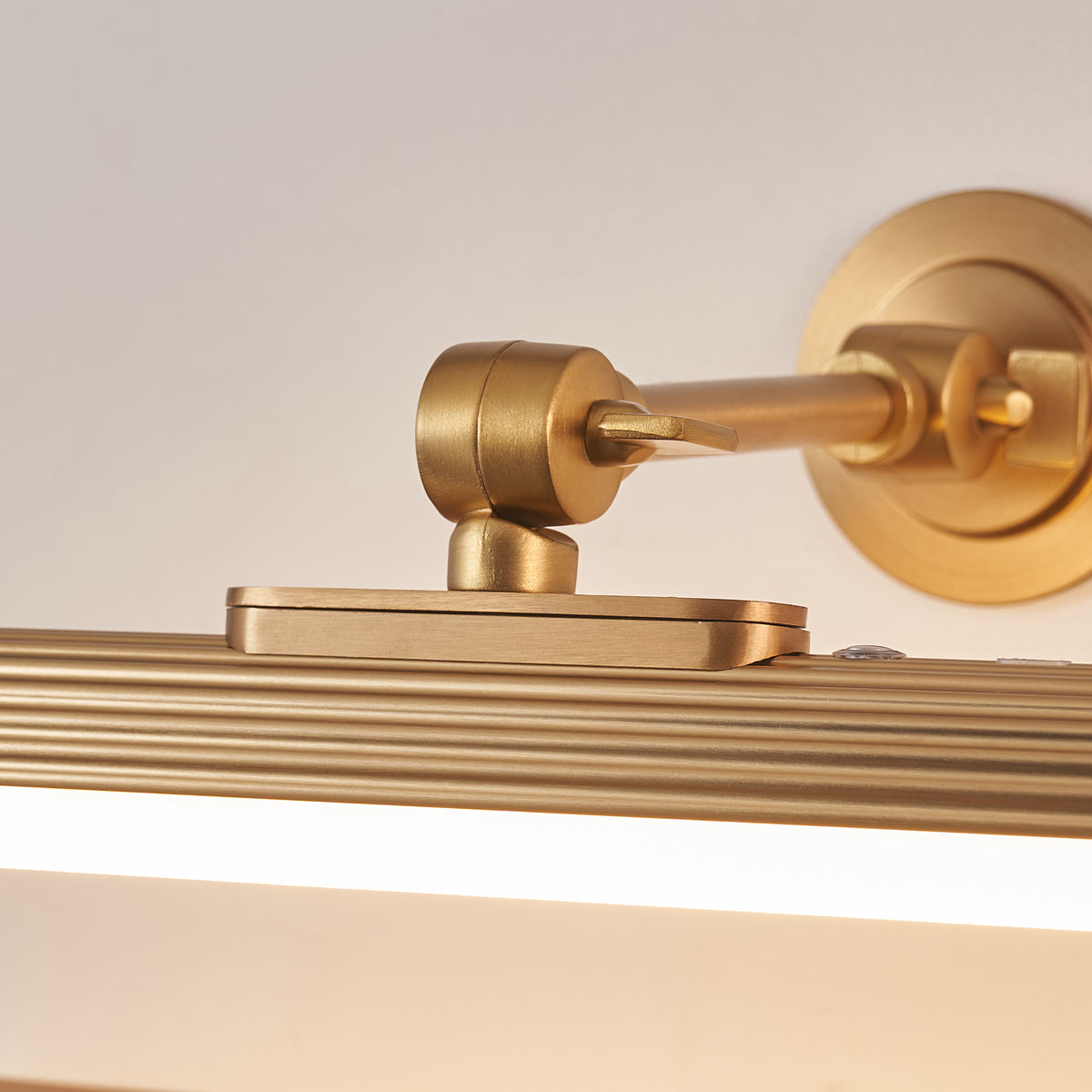 Close-up of the Cirali picture light's brass swivel joint, round wall plate and ribbed tube
