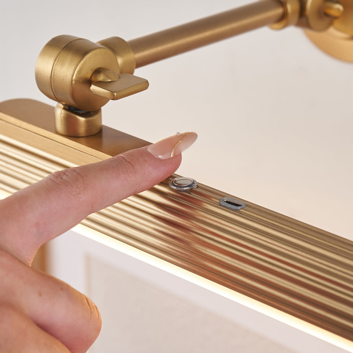 Finger touching the control button on the Cirali picture light's fluted warm brass tube