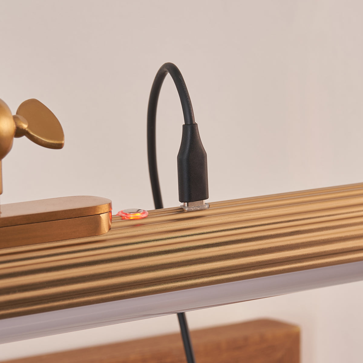 Charging lead attached to the Cirali picture light's ribbed brass tube with indicator light on