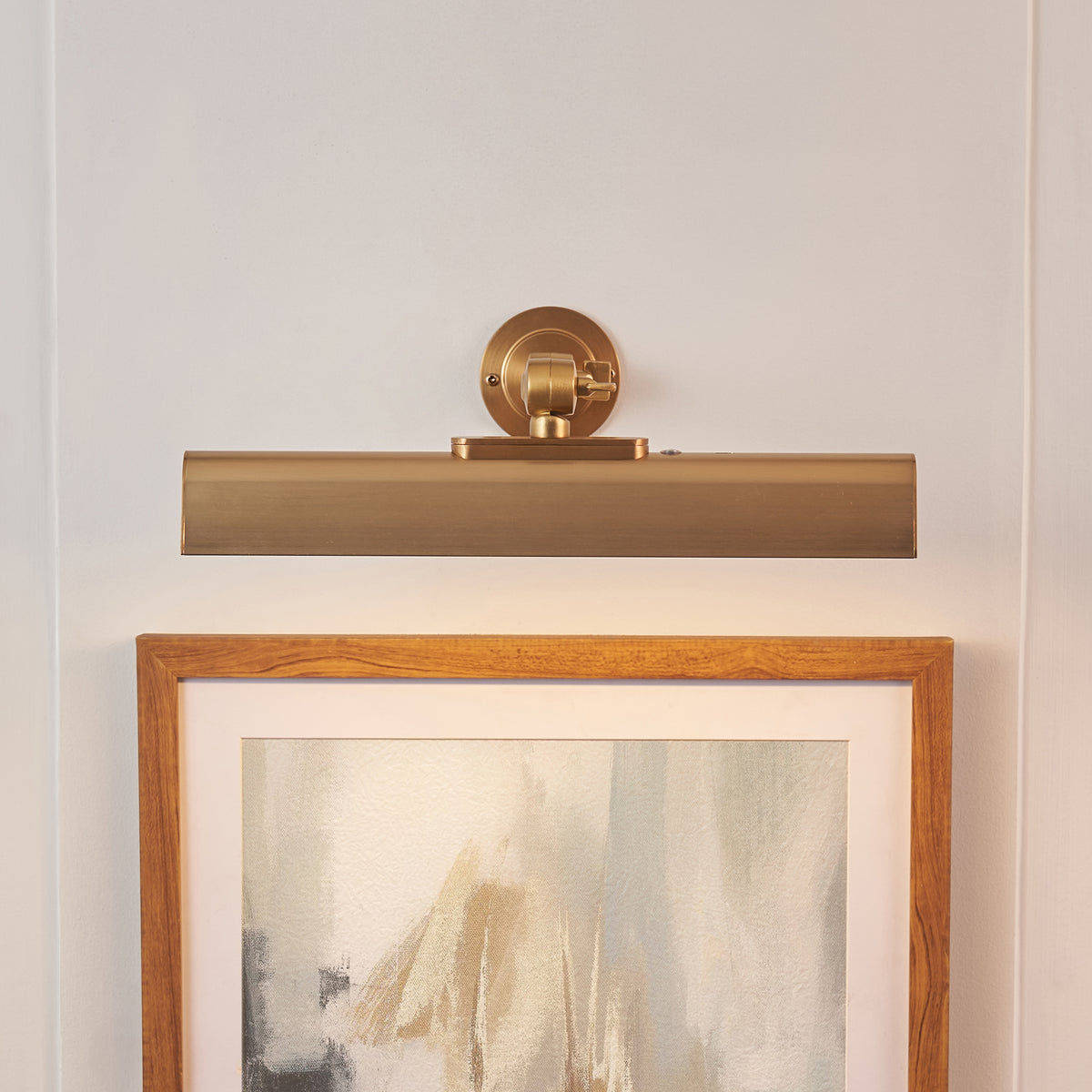Dalyan warm brass picture light mounted above an oak-framed abstract artwork on a white wall